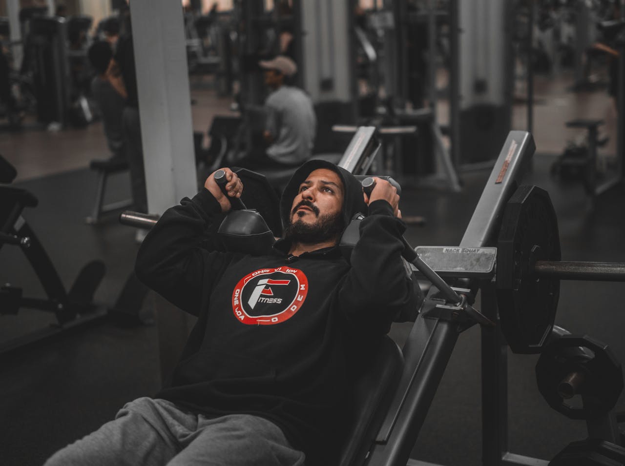 A man focuses intensely while lifting weights on a bench press machine in a modern gym.
